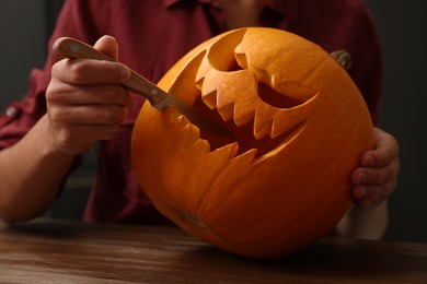 Woman carving pumpkin for Halloween at wooden table, closeup
