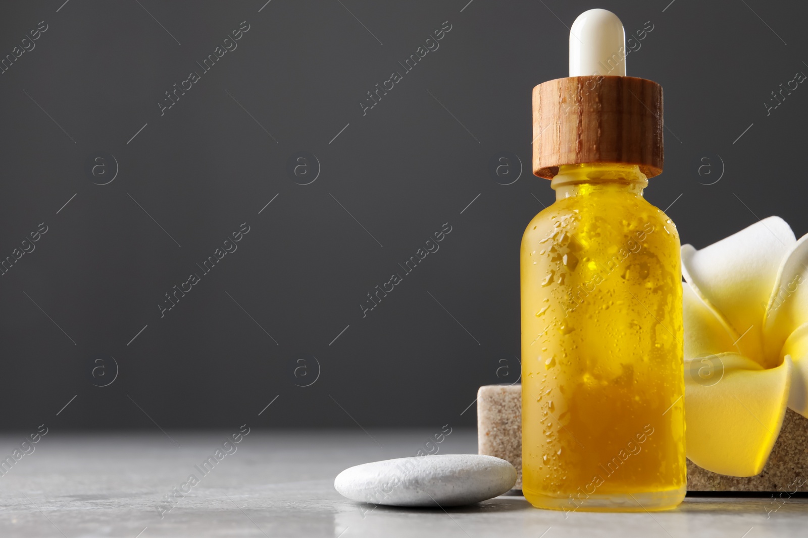 Photo of Bottle of face serum, spa stone and flower on table against grey background, closeup. Space for text