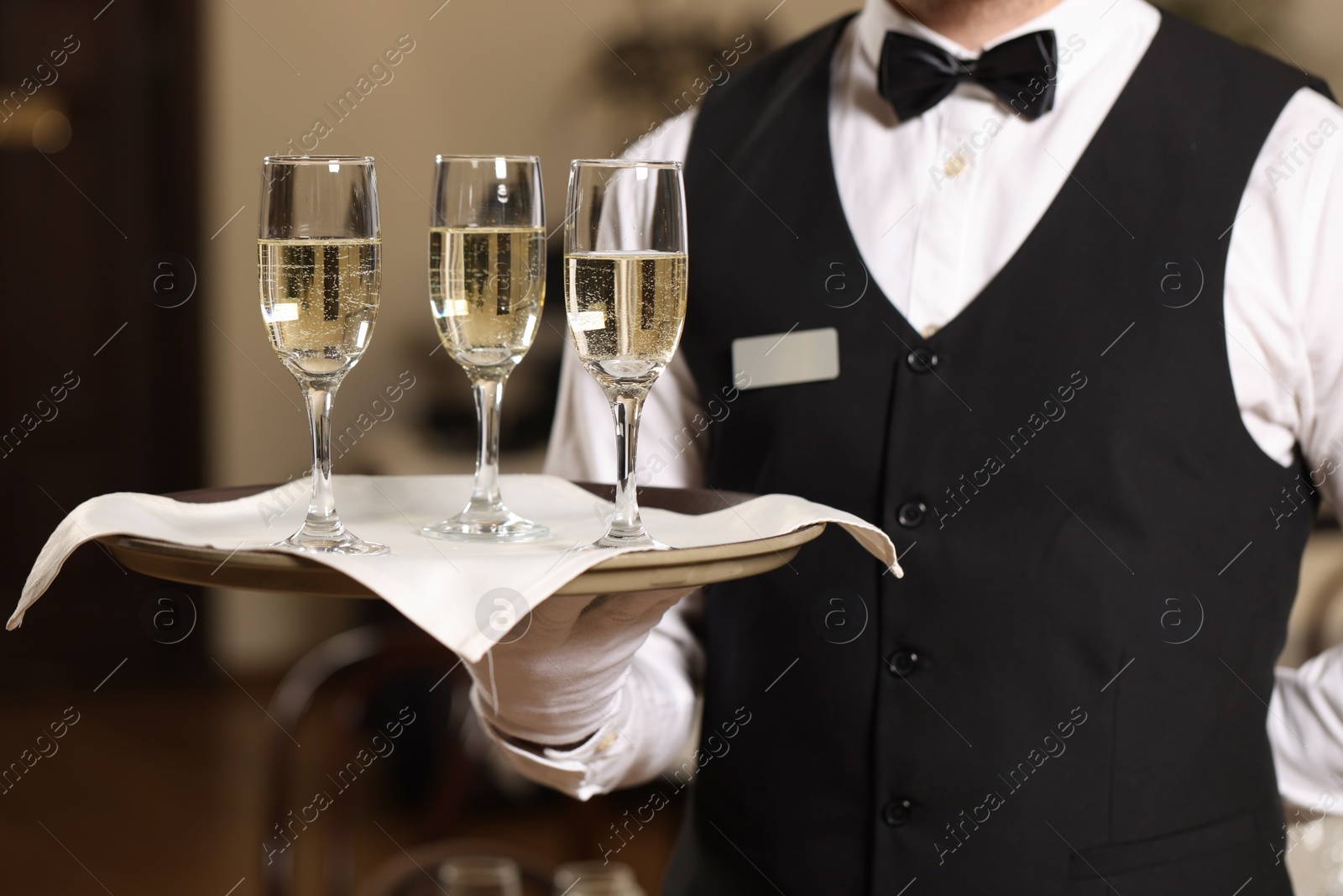 Photo of Butler holding tray with glasses of sparkling wine in restaurant, closeup