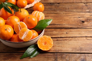 Photo of Fresh tangerines with green leaves in bowl on wooden table, space for text