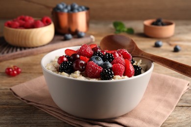 Photo of Bowl with tasty oatmeal porridge and berries served on wooden table. Healthy meal