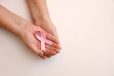 Photo of Senior woman holding pink ribbon on light background, top view with space for text. Breast cancer awareness