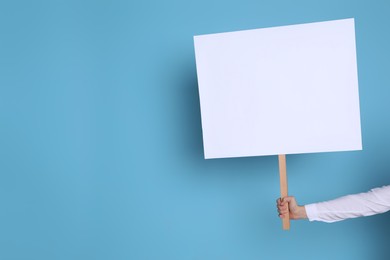 Woman holding blank sign on light blue background, closeup. Space for text