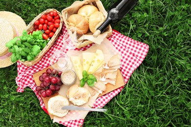 Photo of Picnic blanket with wine and food on green grass, top view