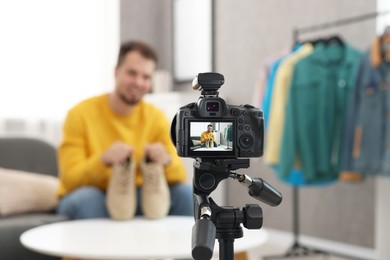 Photo of Fashion blogger showing shoes while recording video at home, focus on camera