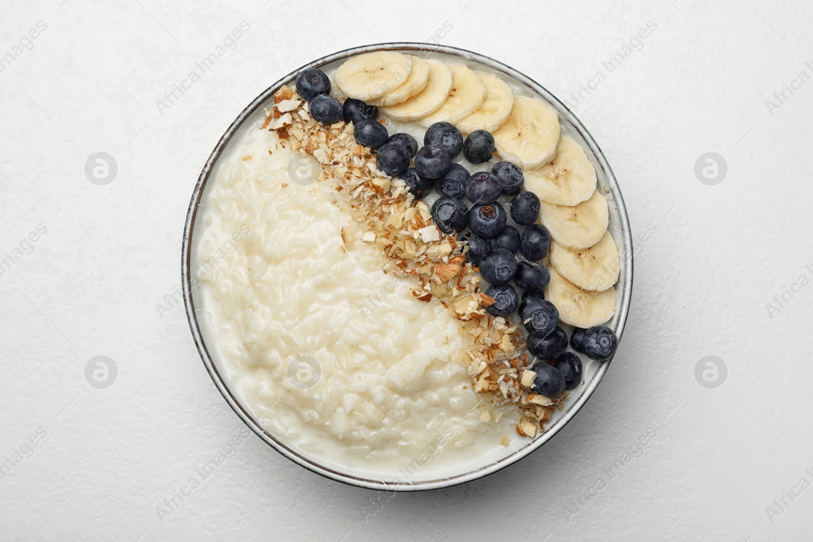 Photo of Delicious rice pudding with banana, blueberries and almond on light table, top view