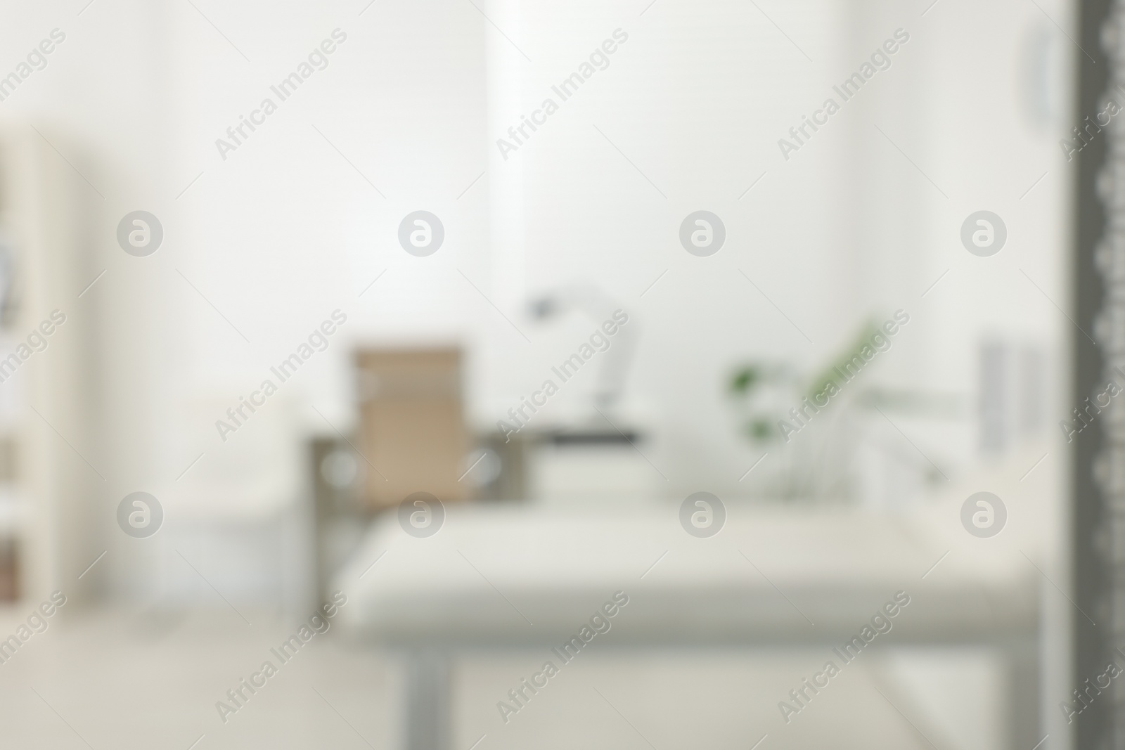 Photo of Blurred view of modern medical office with doctor's workplace and examination table in clinic