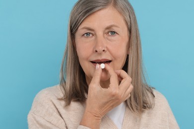 Senior woman taking pill on light blue background
