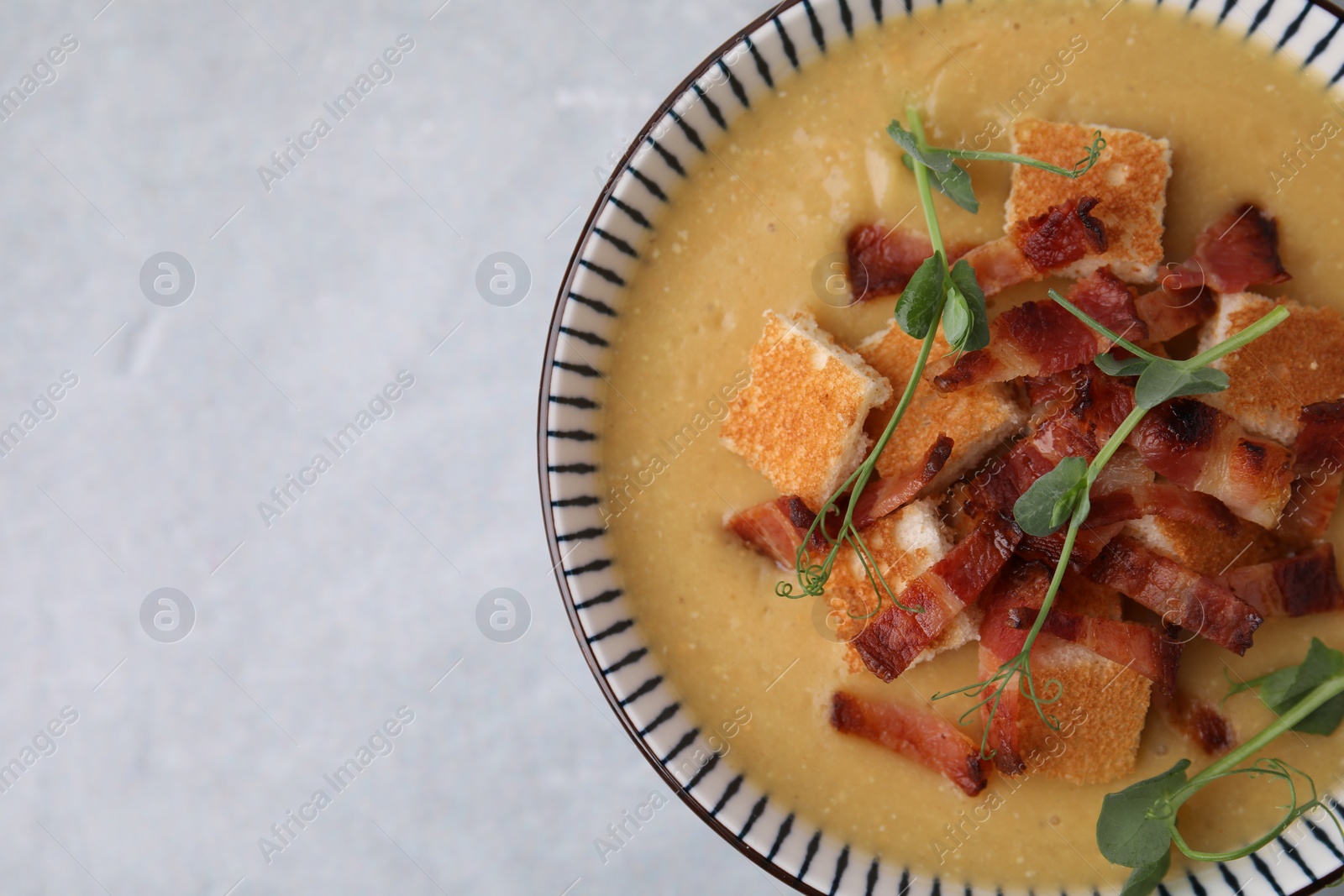 Photo of Delicious lentil soup with bacon and microgreens in bowl on gray table, top view. Space for text