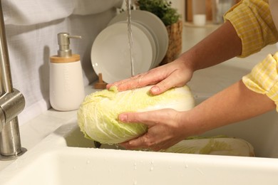 Photo of Woman washing fresh chinese cabbage under tap water in kitchen sink, closeup