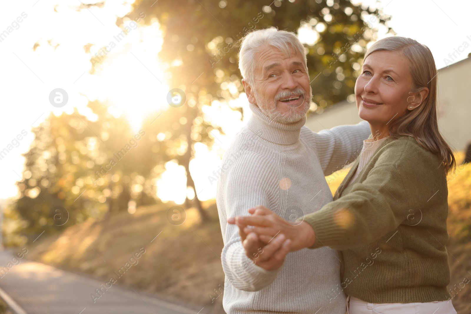 Photo of Affectionate senior couple dancing together outdoors at sunset, space for text