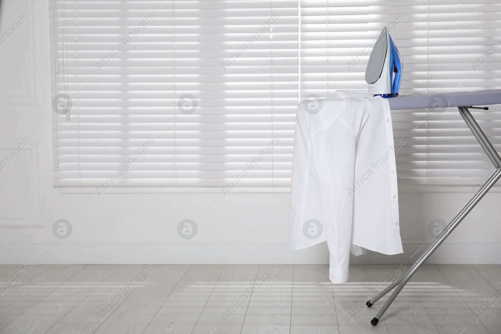 Photo of Modern iron and clean shirt on board indoors, space for text