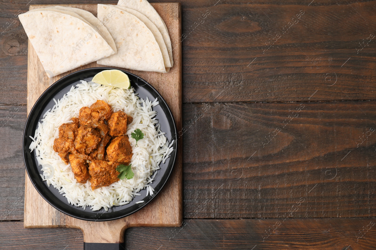 Photo of Delicious chicken curry with rice and tortillas on wooden table, top view. Space for text