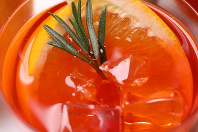 Photo of Aperol spritz cocktail, ice cubes, rosemary and orange slices in glass, closeup