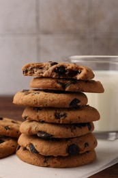 Photo of Stack of delicious chocolate chip cookies and milk on wooden table, closeup