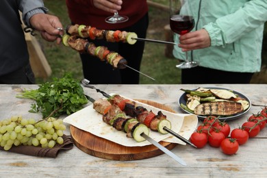 Photo of Friends having barbecue party outdoors, focus on table with delicious food