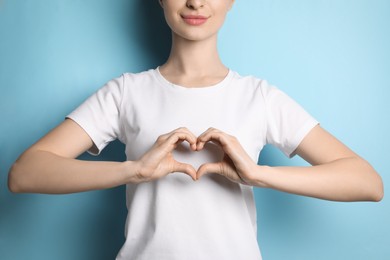 Photo of Woman making heart with hands on light blue background, closeup