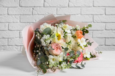 Bouquet of beautiful flowers on wooden table against white brick wall