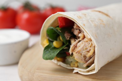Photo of Delicious tortilla wrap with tuna on wooden board, closeup