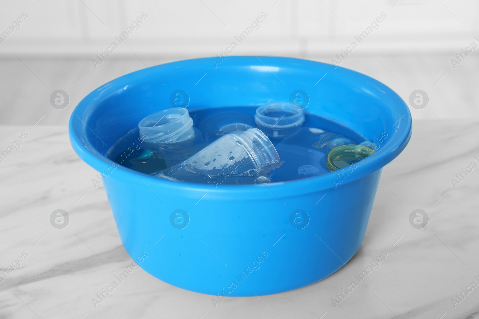 Photo of Basin with baby bottles and nipples on white marble table in kitchen