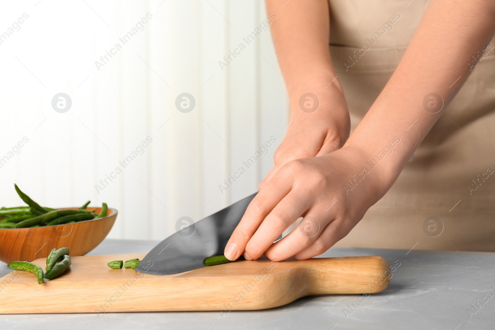 Photo of Woman cutting raw green beans for tasty dish at table