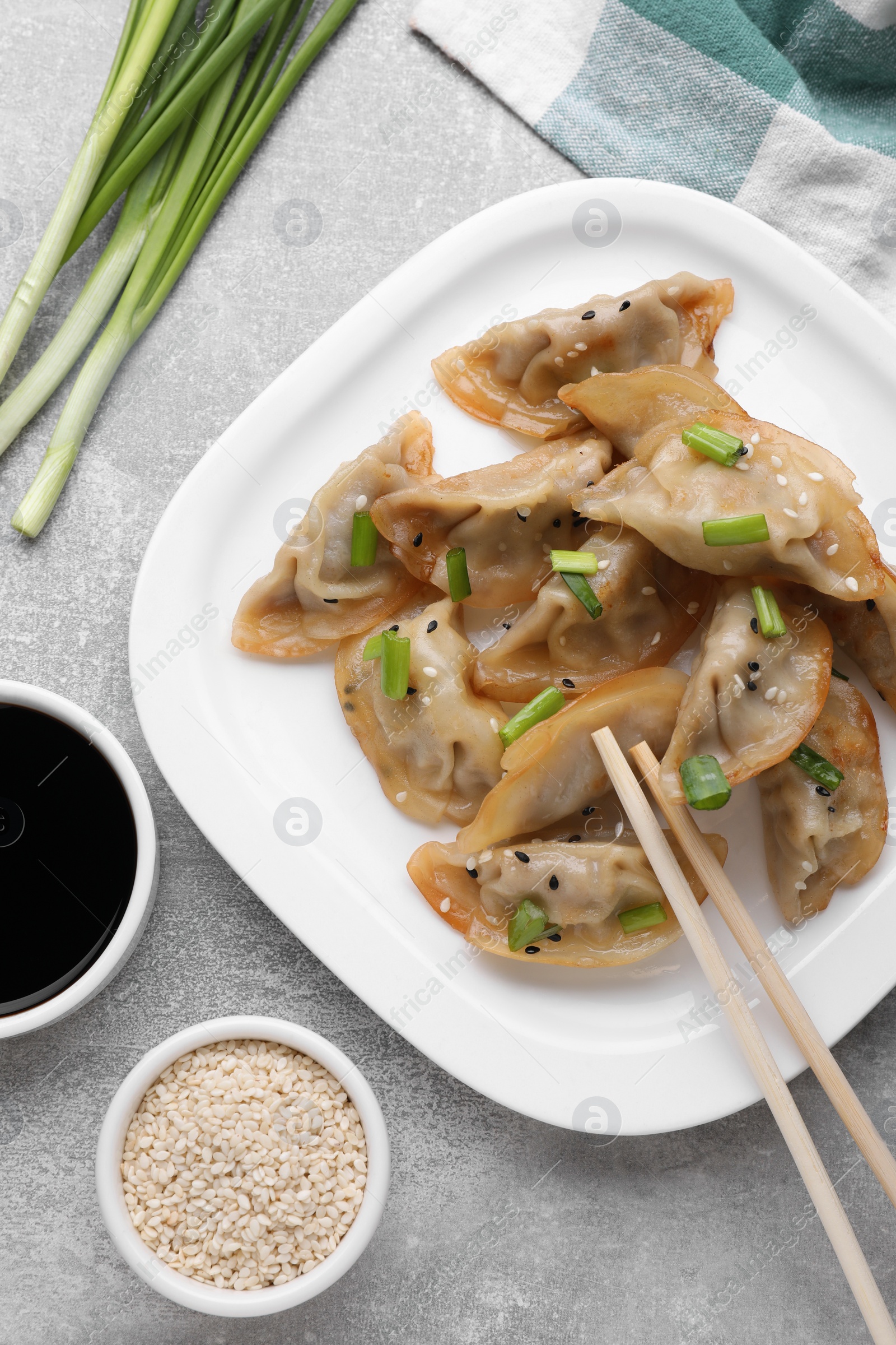 Photo of Delicious gyoza (asian dumplings) with green onions, sesame, soy sauce and chopsticks on light gray table, flat lay