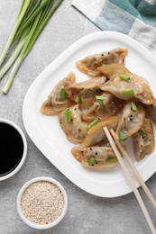 Delicious gyoza (asian dumplings) with green onions, sesame, soy sauce and chopsticks on light gray table, flat lay