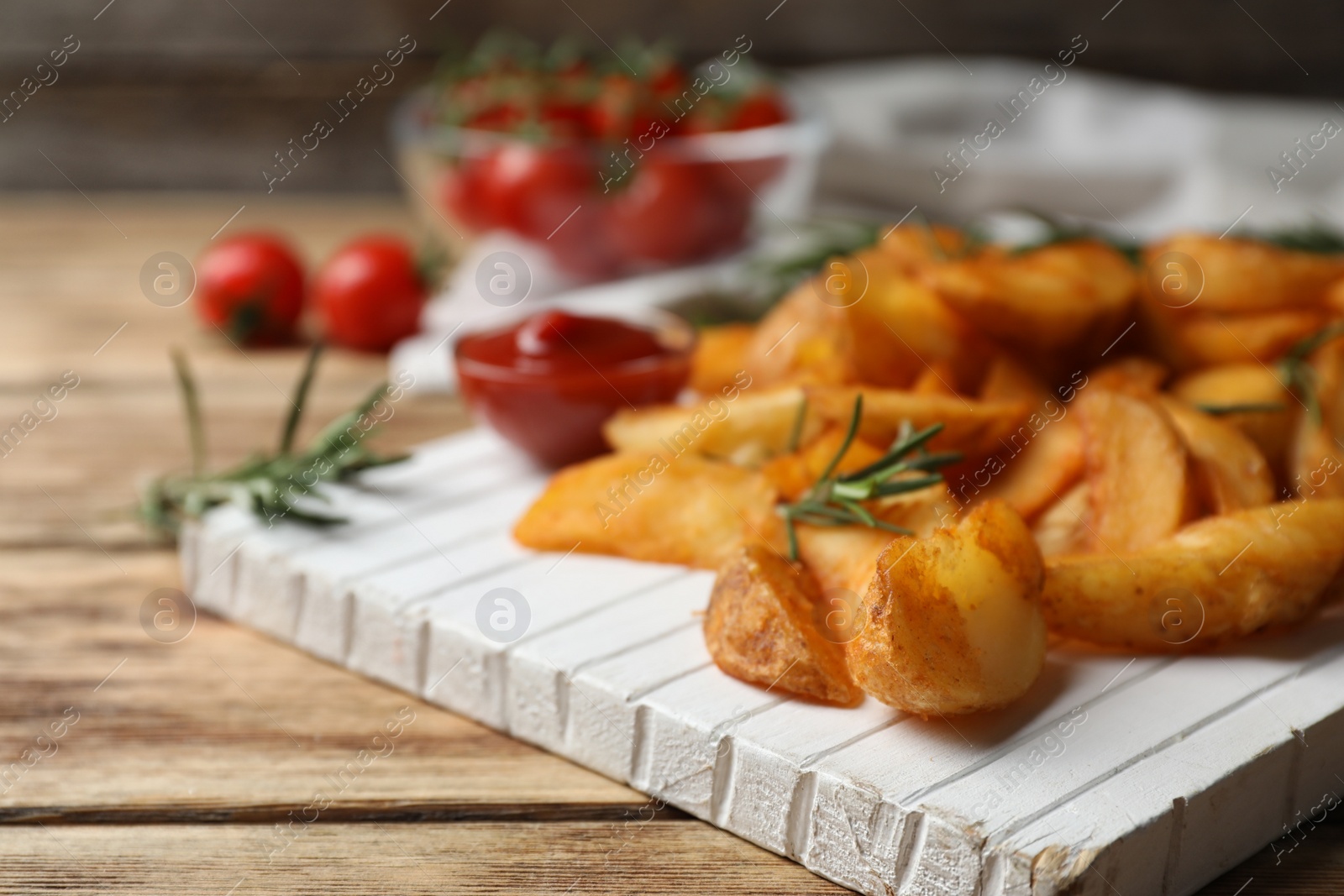 Photo of Wooden board with baked potatoes and rosemary on table, closeup