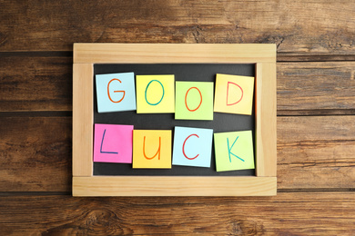 Notes with phrase GOOD LUCK on wooden background, top view