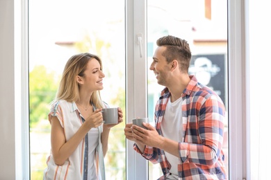 Photo of Happy young couple drinking morning coffee near window at home