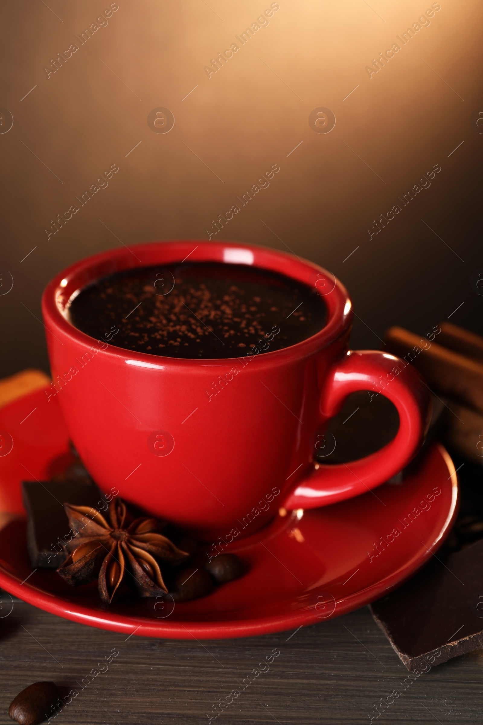 Photo of Cup of delicious hot chocolate, spices and coffee beans on wooden table