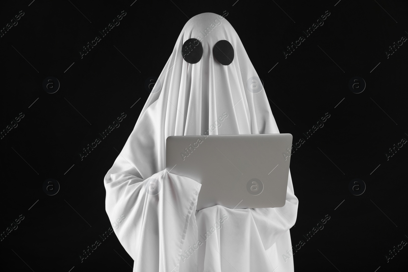 Photo of Creepy ghost. Person in white sheet with laptop on black background