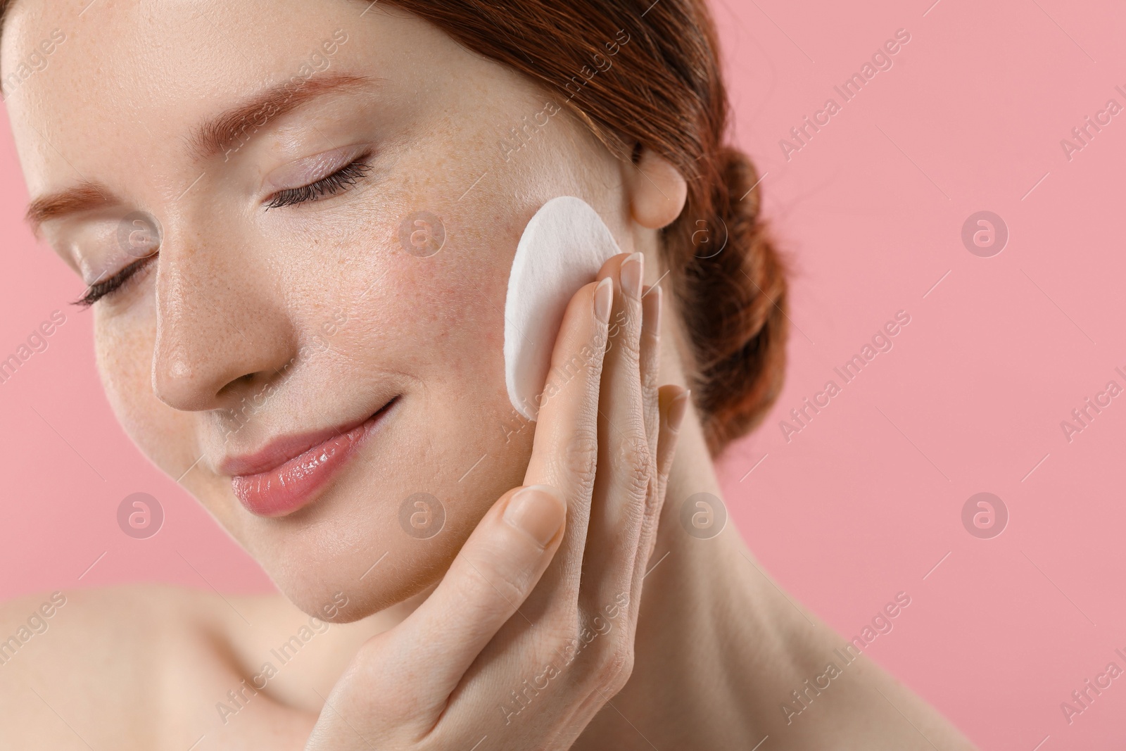 Photo of Beautiful woman with freckles wiping face on pink background, closeup