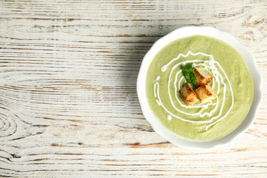 Delicious broccoli cream soup with croutons served on white wooden table, top view. Space for text