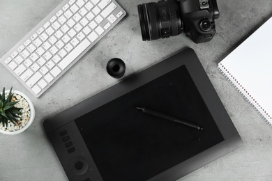 Flat lay composition with graphic tablet and camera on grey stone table, space for text. Designer's workplace