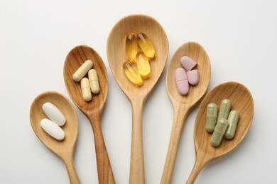 Photo of Vitamin capsules in wooden spoons on white background, flat lay