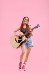 Photo of Stylish young hippie woman playing guitar on pink background