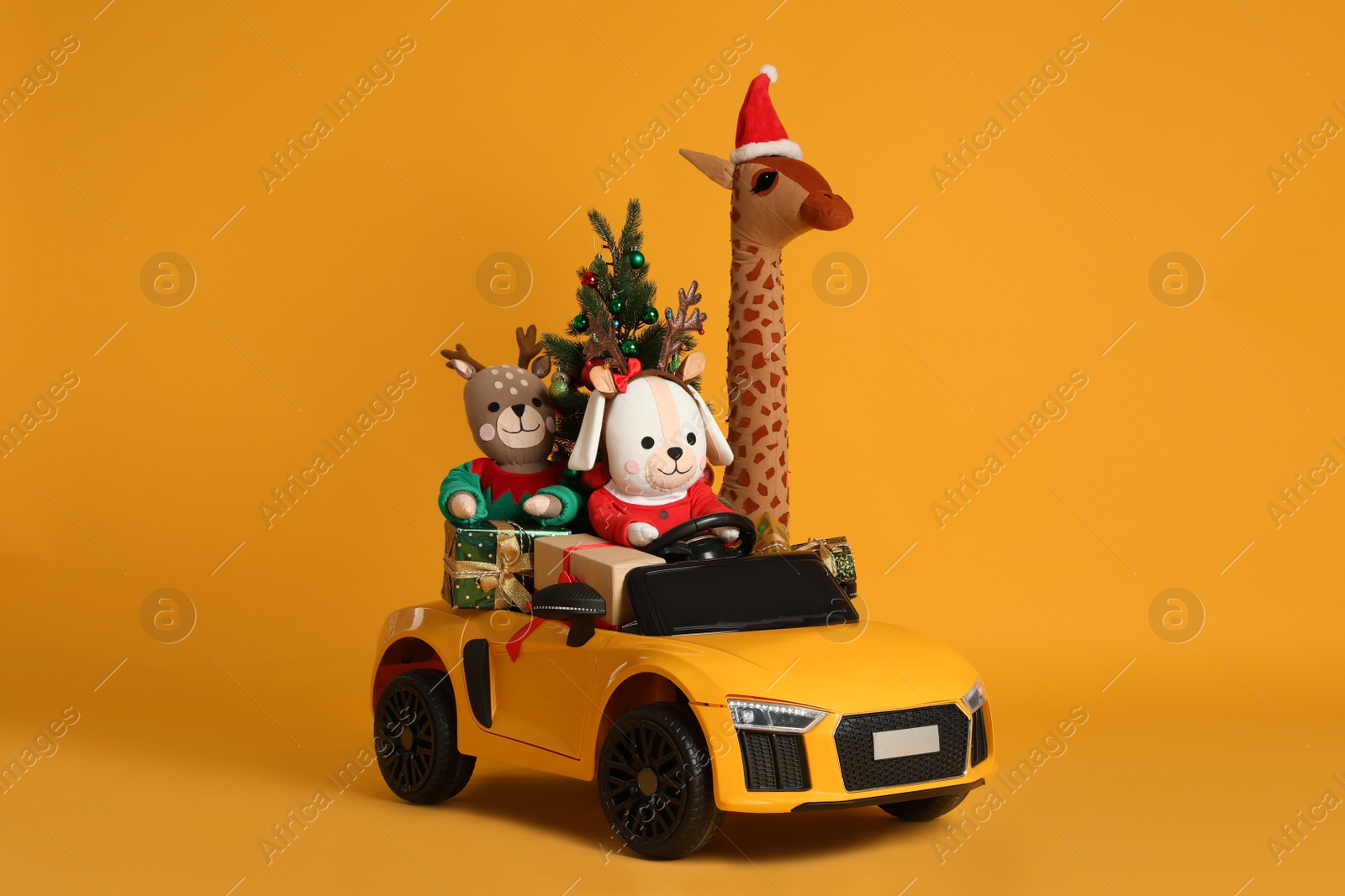 Photo of Child's electric car with toys, gift boxes and Christmas tree on orange background