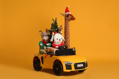 Child's electric car with toys, gift boxes and Christmas tree on orange background