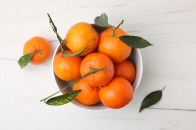 Photo of Bowl with fresh ripe tangerines and leaves on white wooden table, top view
