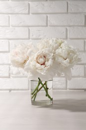 Photo of Beautiful peonies in glass vase on white table near brick wall