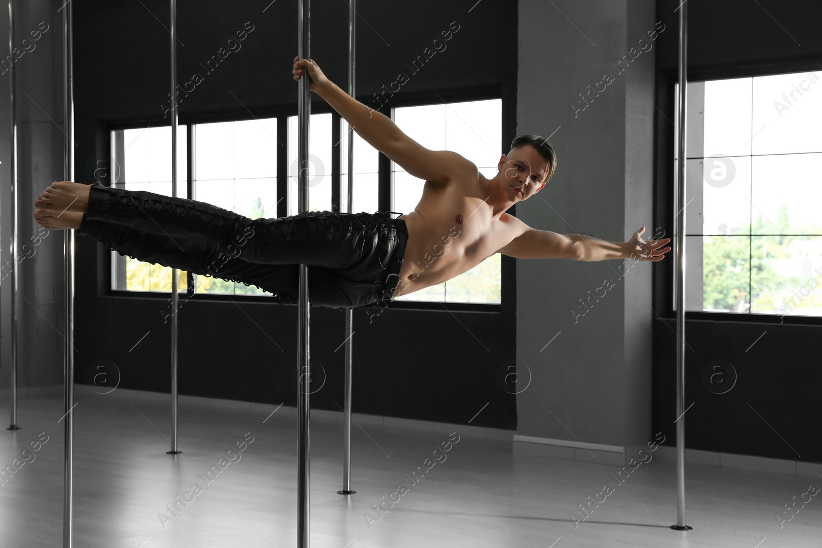 Photo of Attractive young man dancing in studio with poles