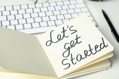 Photo of Notebook with phrase Let's Get Started and keyboard on white table
