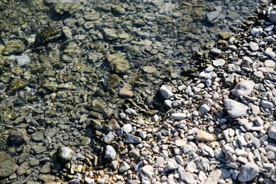 Photo of River coast with stones and pebbles on sunny day