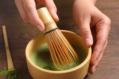 Photo of Woman preparing matcha tea at wooden table, closeup