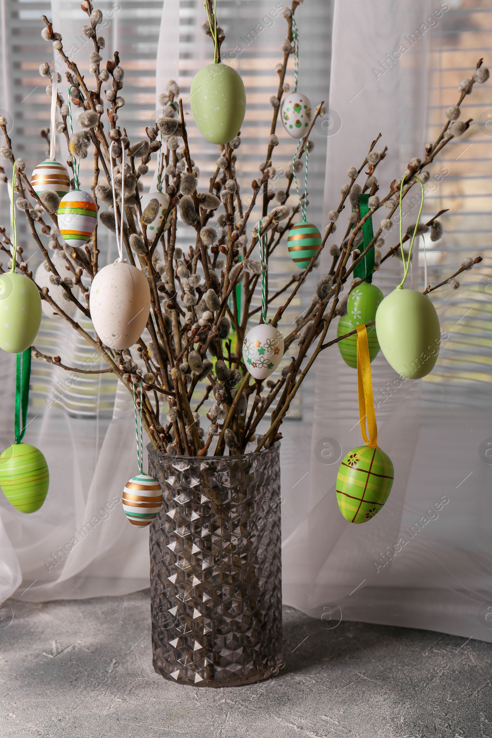 Photo of Beautiful willow branches with painted eggs in vase on light grey table. Easter decor