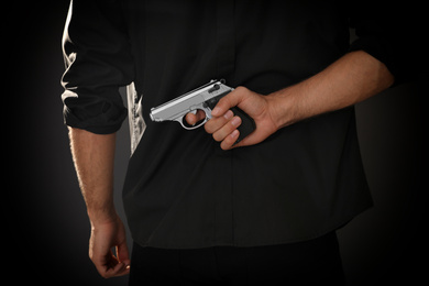 Photo of Professional killer with gun on black background, closeup