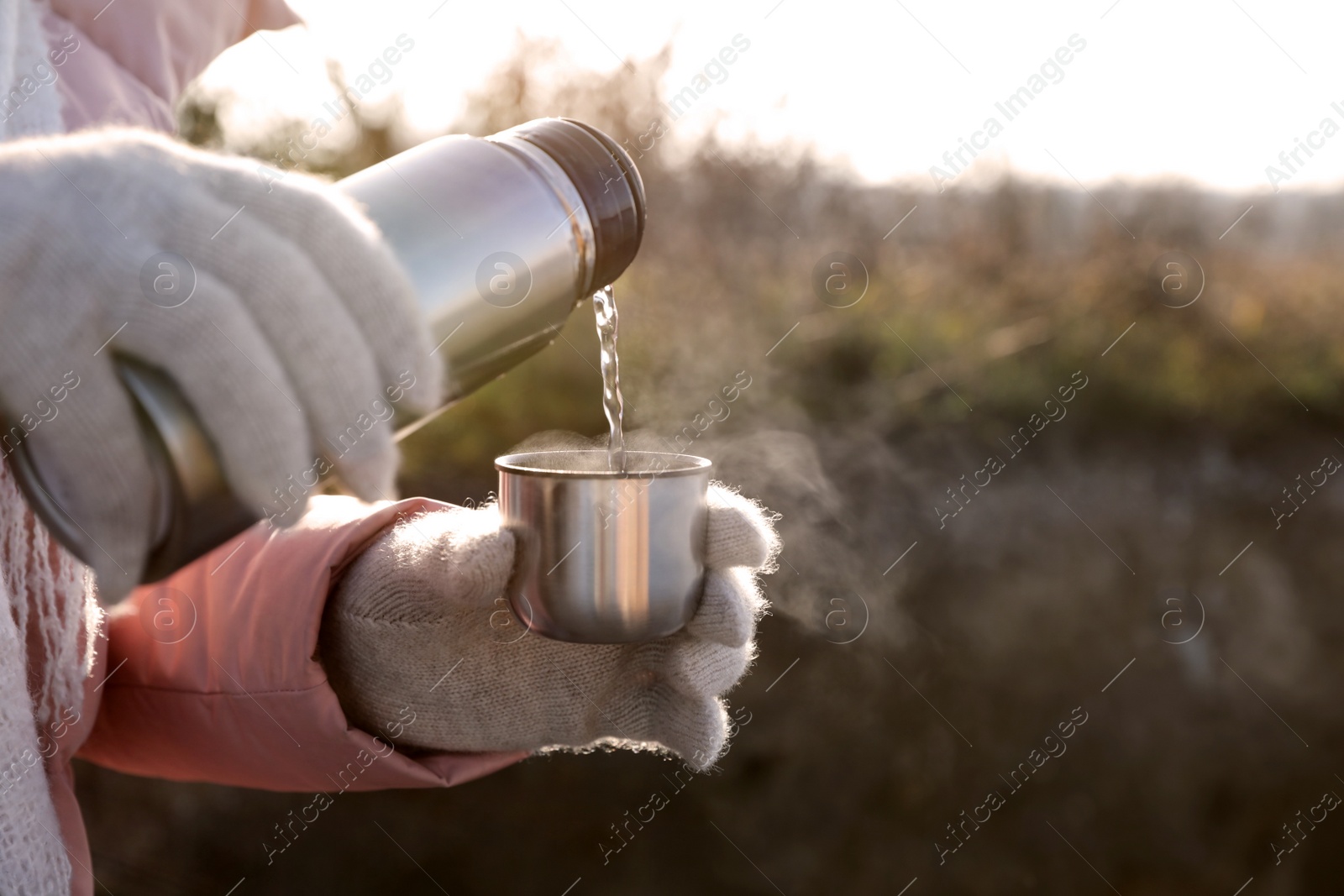 Photo of Woman pouring hot drink into cup from thermos outdoors, closeup