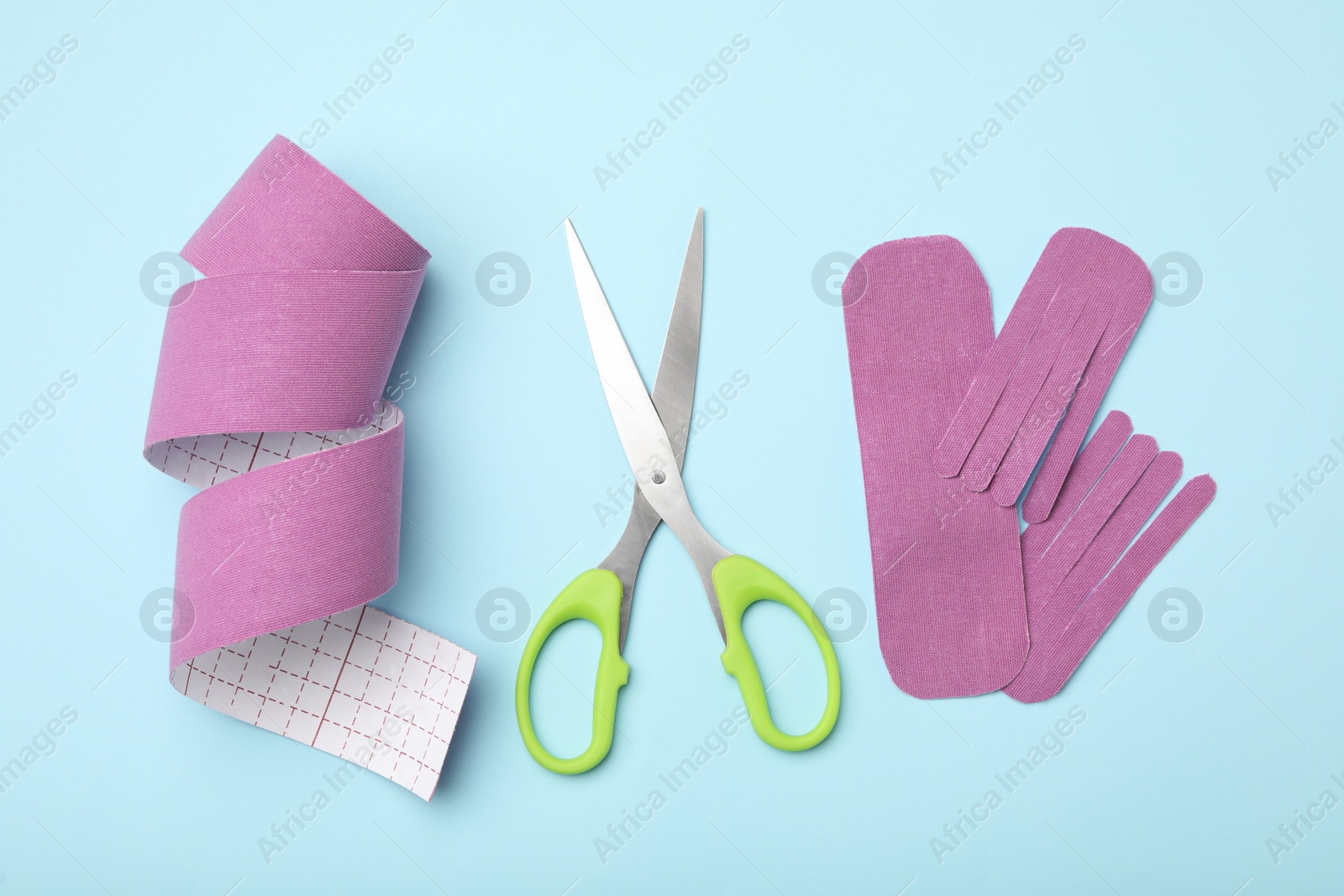 Photo of Bright kinesio tape pieces and scissors on light blue background, flat lay