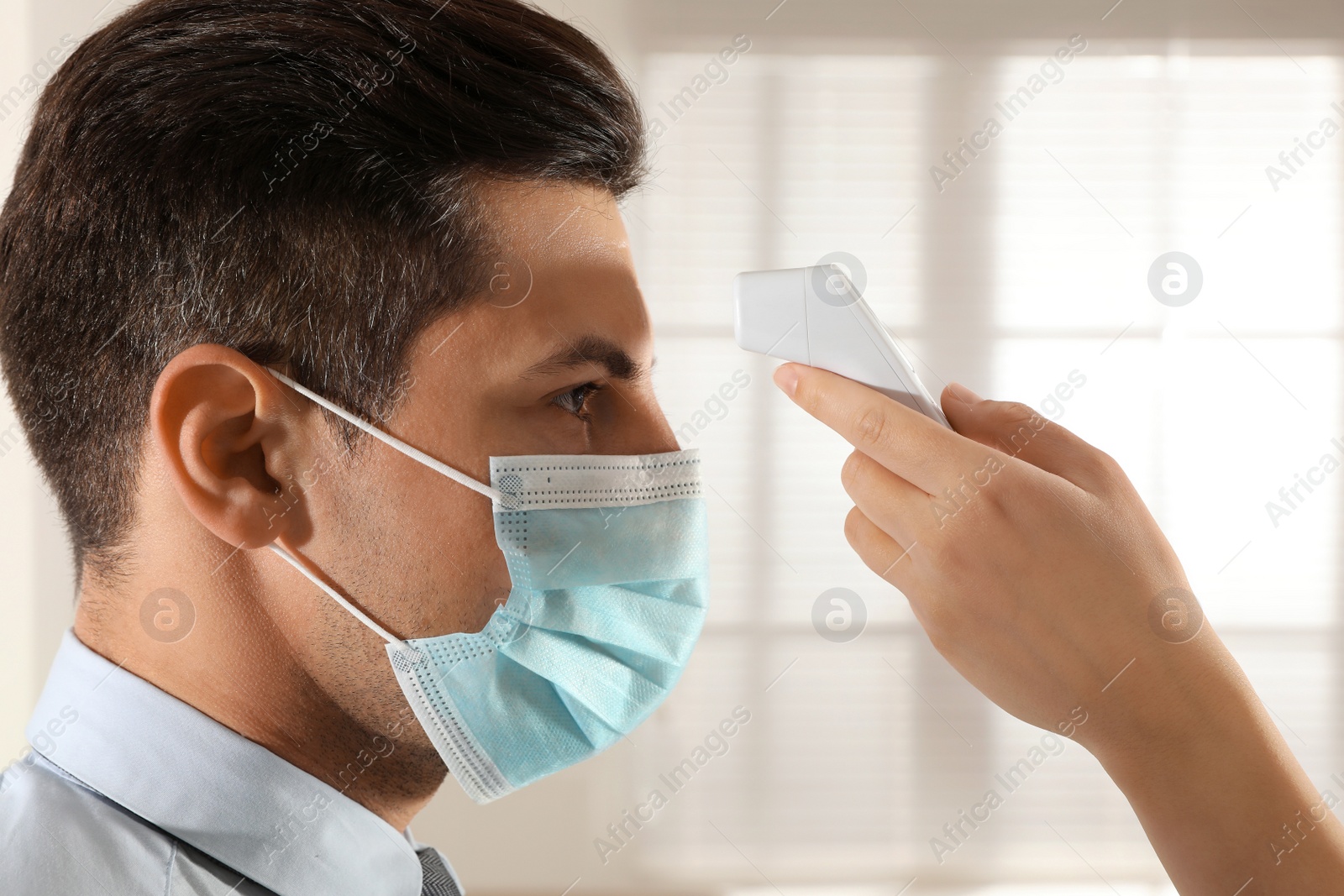 Photo of Doctor measuring man's temperature in office closeup. Prevent spreading of Covid-19